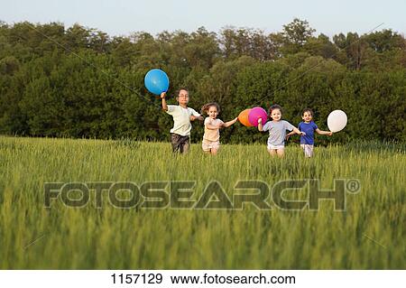 Stock Photo - Children running in a field with balloons. Fotosearch