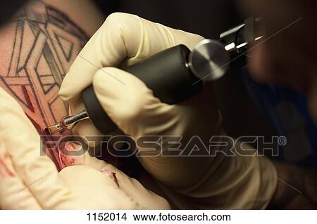 Picture - Close-up of a tattoo artist tattooing a design on human skin. Fotosearch