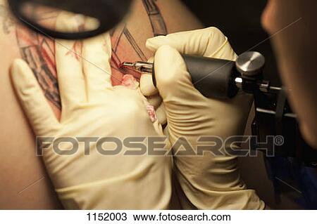 Stock Image - Close-up of a tattoo artist tattooing a design on human skin. Fotosearch