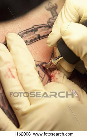 Stock Photo - Close-up of a tattoo artist tattooing a design on human skin. Fotosearch