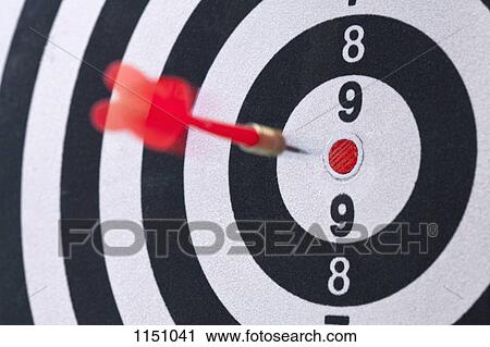 Stock Image - Close-up, rear view of dart flying into a target. Fotosearch