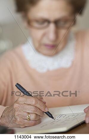 Picture - Detail of a senior woman writing in a note book. Fotosearch