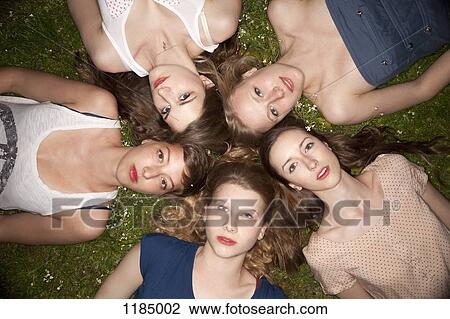 Stock Image - Five female friends lying in the grass in a circle looking sensually at the camera. Fotosearch