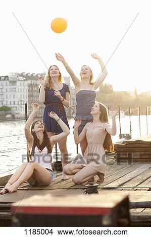Picture - Four female friends tossing a ball around on a jetty next to Spree River, Berlin, Germany. Fotosearch