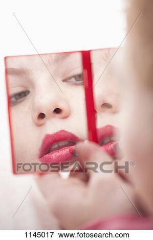 Stock Photo - Girl holding hand mirror and applying lipstick . Fotosearch
