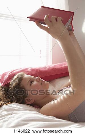 Stock Image - Girl lying on bed reading book. Fotosearch