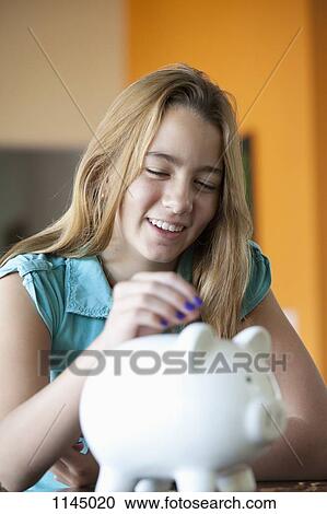 Stock Image - Girl putting coin in piggy bank. Fotosearch