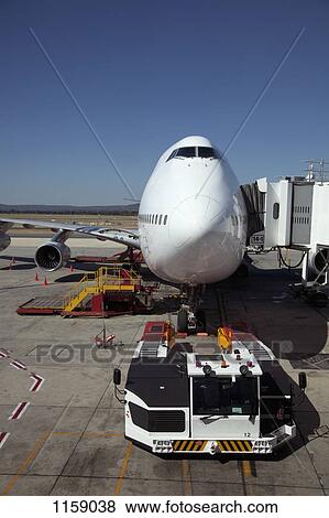 Stock Photo - Jumbo jet attached to boarding bridge with tug in front . Fotosearch