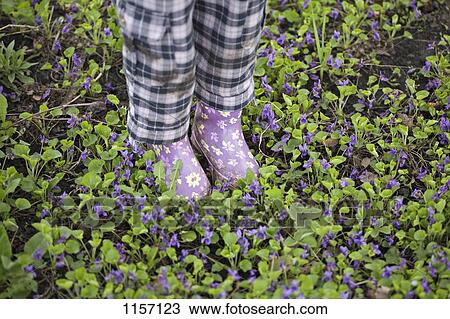 Stock Image - Low section of a girl standing in a garden with gumboots. Fotosearch