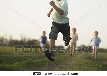 Stock Image - Low view of a boy running in a field with other children behind. Fotosearch