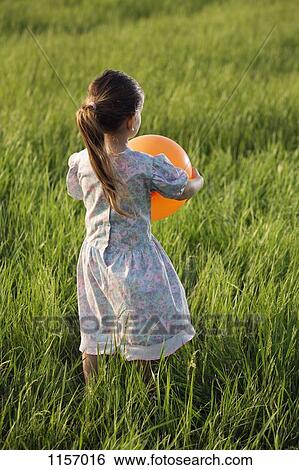 Stock Photograph - Rear view of a girl holding a balloon in a field. Fotosearch