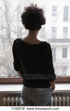 Rear view of a woman looking through a window View Large Photo Image Stock Photo - Rear view of a woman looking through a window. Fotosearch