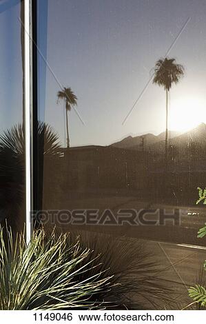 Stock Photograph - Reflection of mountains, palm trees and a house in a window. Fotosearch