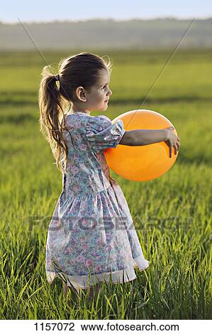 Side view of a girl holding a balloon in a field View Large Photo Image Stock Image - Side view of a girl holding a balloon in a field. Fotosearch