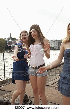 Stock Photo - Three female friends looking at bubbles on the Spree River, Berlin, Germany. Fotosearch