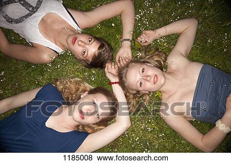 Stock Photo - Three female friends lying in the grass in a circle looking sensually at the camera. Fotosearch