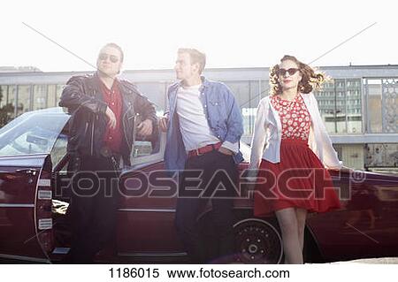 Stock Photography - Three rockabilly friends leaning against a vintage car. Fotosearch