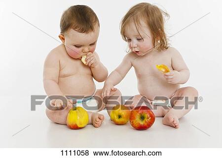Two baby girls sitting together eating apples View Large Photo Image Stock Photo - Two baby girls sitting together eating apples. Fotosearch