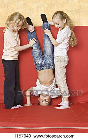 Stock Image - Two girls holding a boy upside down. Fotosearch