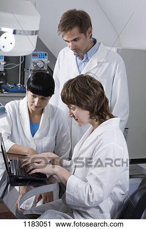 Two lab technicians watching as a third tech types notes on a laptop View Large Photo Image Stock Image - Two lab technicians watching as a third tech types notes on a laptop. Fotosearch