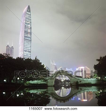 Stock Photo - View of illuminated city buildings across water at night, Shenzhen, China. Fotosearch