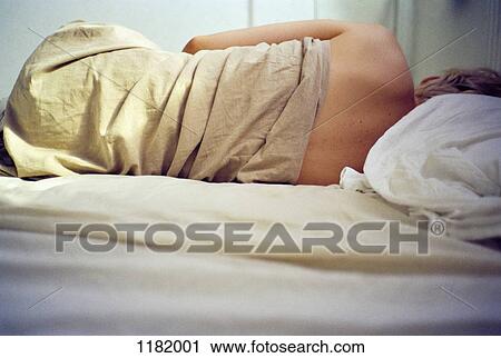 Stock Image - Woman in bed wrapped in crumpled sheet. Fotosearch