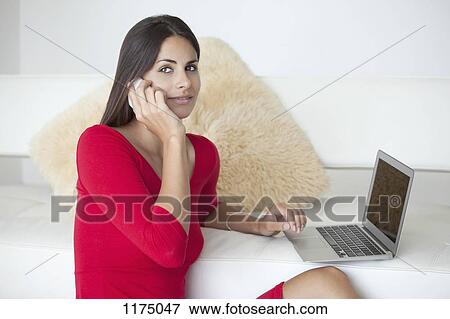 Stock Photo - Woman in red on phone with laptop. Fotosearch