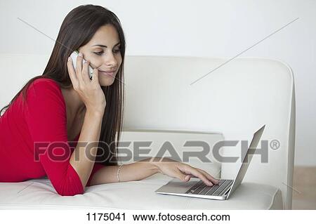 Stock Image - Woman in red using phone and laptop. Fotosearch