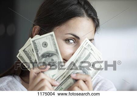 Picture - Woman peeking behind hundred dollar bills. Fotosearch