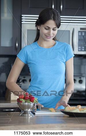 Stock Image - Woman slicing melon in kitchen. Fotosearch