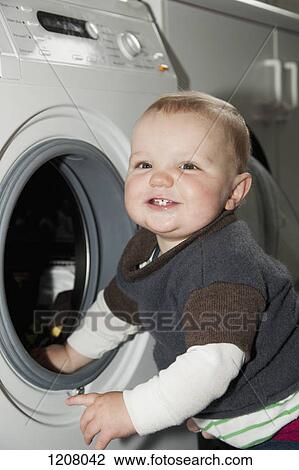 Stock Image - A baby boy standing next to a washing machine. Fotosearch