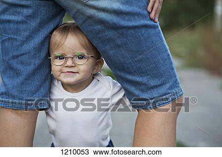 Stock Image - A baby girl holding herself up in between her mother's legs . Fotosearch