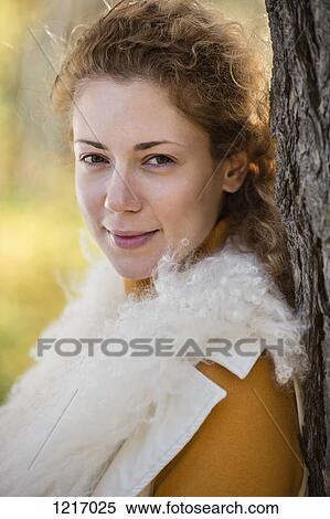 Stock Photography - A beautiful woman leaning against a tree in autumn. Fotosearch