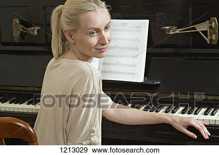 Stock Photo - A beautiful woman sitting at a piano. Fotosearch