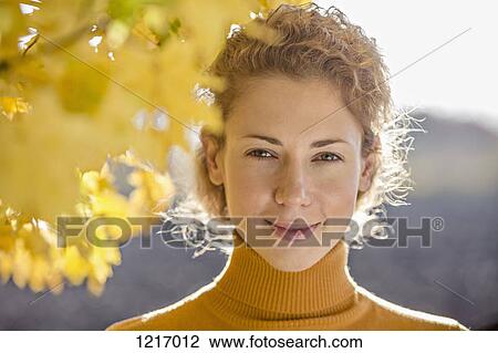 Stock Image - A beautiful woman standing near a tree in autumn. Fotosearch