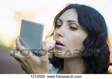 A beautiful young woman applying lipstick using a compact mirror View Large Photo Image Stock Photograph - A beautiful young woman applying lipstick using a compact mirror. Fotosearch