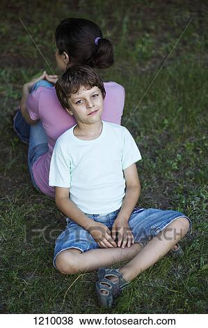 A boy sitting cross-legged on grass, leaning his back against his mom's back View Large Photo Image Stock Photo - A boy sitting cross-legged on grass, leaning his back against his mom's back. Fotosearch