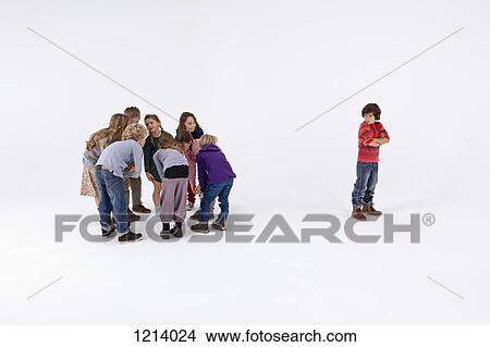 A boy standing alone, arms crossed, while a group of kids gossip about him View Large Photo Image Picture - A boy standing alone, arms crossed, while a group of kids gossip about him. Fotosearch