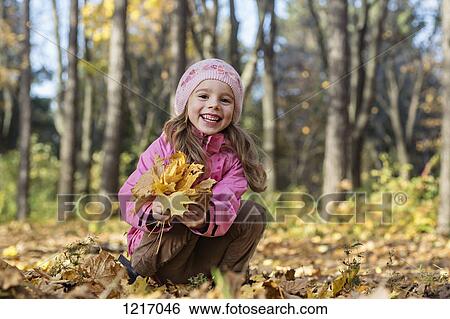 A cheerful girl picking up autumn leaves in a wooded area View Large Photo Image Stock Photograph - A cheerful girl picking up autumn leaves in a wooded area. Fotosearch