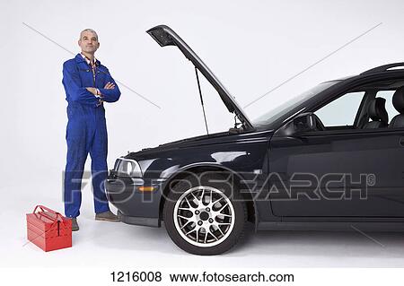 A confident auto mechanic standing with arms crossed next to a car with open hood View Large Photo Image Stock Photo - A confident auto mechanic standing with arms crossed next to a car with open hood. Fotosearch