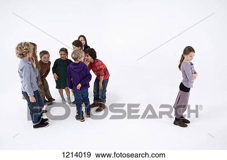 Stock Photo - A girl standing alone, arms crossed, while a group of kids gossip about her. Fotosearch