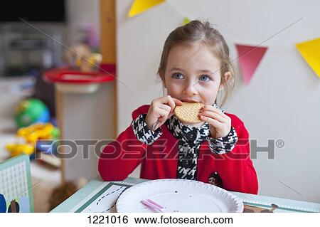 A little girl sitting at a table, taking a bite out of a cookie View Large Photo Image Stock Photograph - A little girl sitting at a table, taking a bite out of a cookie. Fotosearch