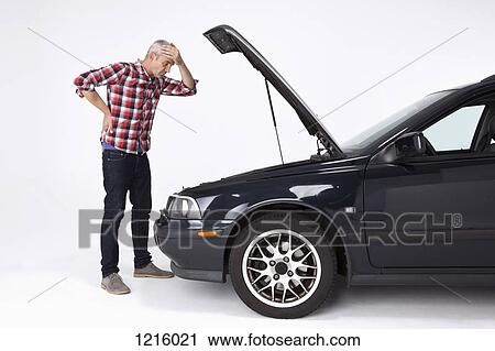 A man standing next to a broke down car, looking down at engine in frustration View Large Photo Image Stock Image - A man standing next to a broke down car, looking down at engine in frustration. Fotosearch