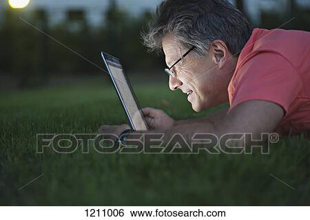 A mature man lying in the grass using a laptop View Large Photo Image Stock Photograph - A mature man lying in the grass using a laptop. Fotosearch