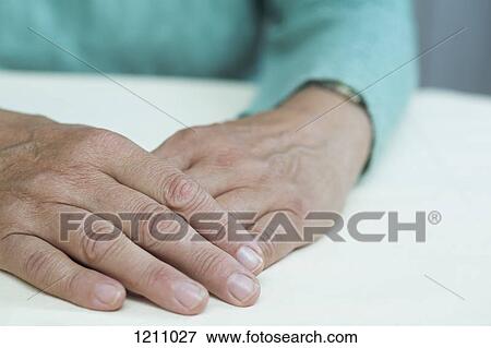Stock Photo - A mature woman sitting at a table, close-up of hands. Fotosearch