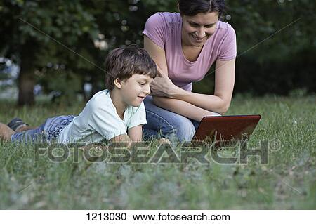 A mother and her son laughing while watching something on a laptop in a park View Large Photo Image Stock Image - A mother and her son laughing while watching something on a laptop in a park. Fotosearch