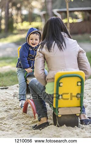 Stock Photograph - A mother and her son on a seesaw at a playground. Fotosearch