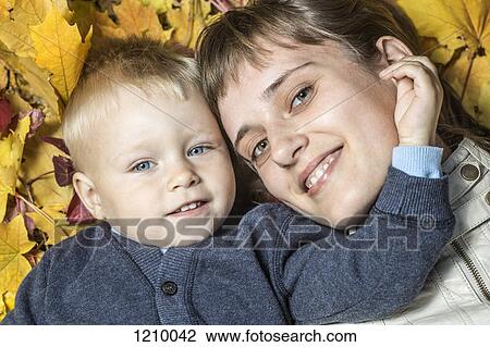 Stock Image - A mother and her young son lying side by side in autumn leaves. Fotosearch