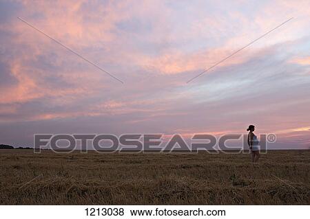 Stock Photo - A pregnant woman standing in a remote field under a dramatic sky. Fotosearch