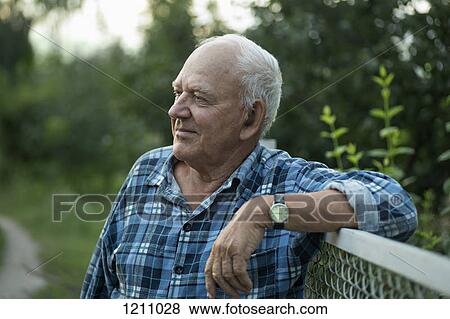 Stock Photo - A senior man leaning on a fence and looking away serenely. Fotosearch